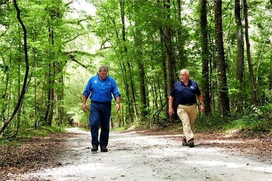 Two men walking along a trail under lush trees
